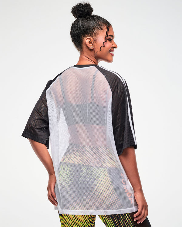 Shown from the back, female model wearing a white mesh oversized tee with black and white striped sleeves, paired with colorful dot-print leggings.