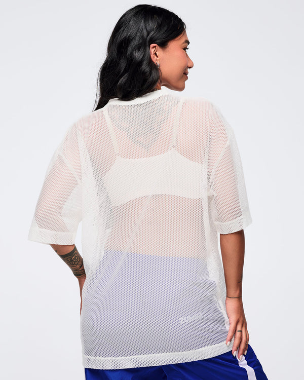 Back view of the white mesh short-sleeve V-neck top showing the sheer mesh panel and relaxed sleeves, modeled by a female wearing blue track pants on a white studio background.