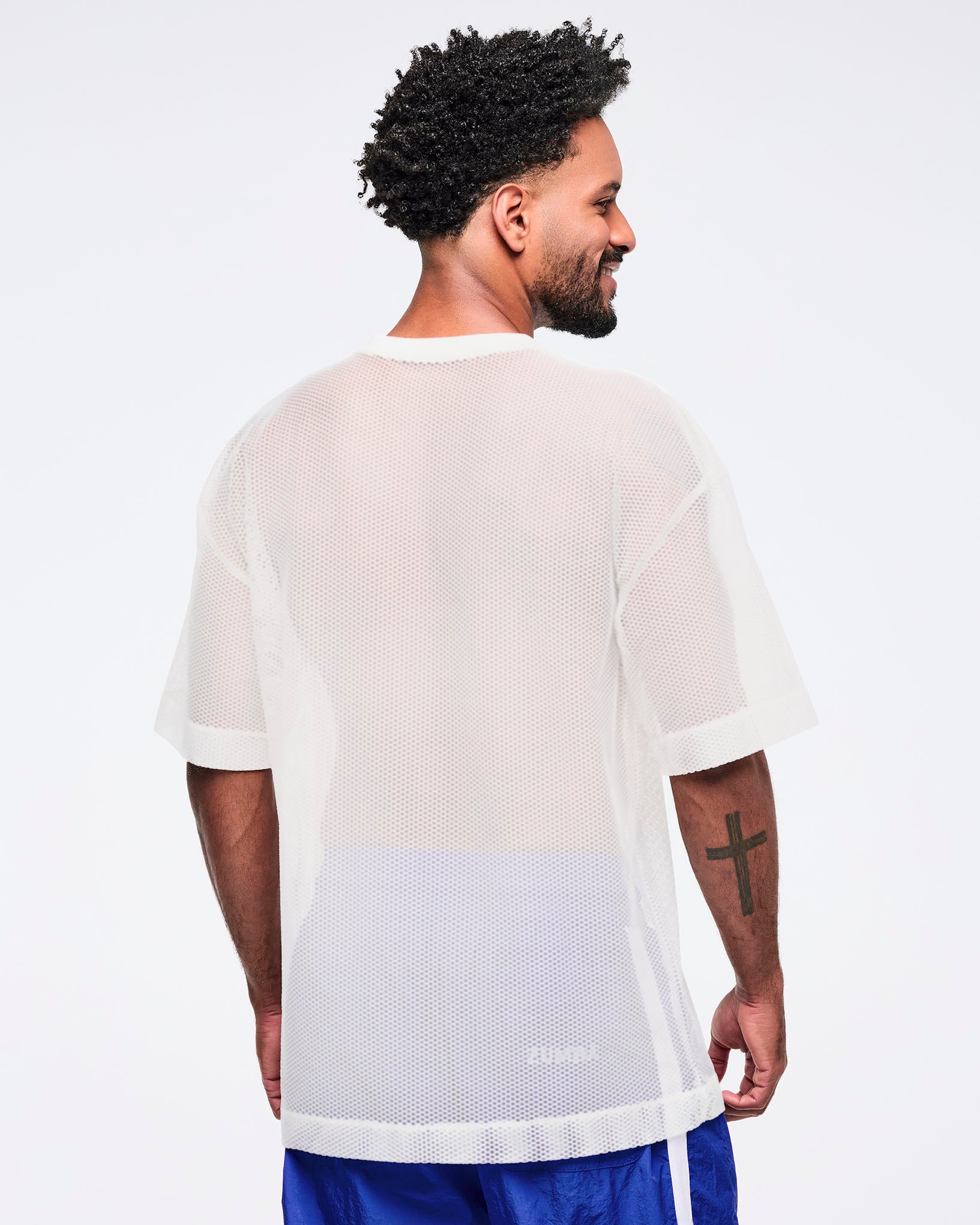 Back view of the white mesh short-sleeve V-neck top showing a sheer, breathable mesh texture, modeled by a male wearing blue track pants on a white studio background.