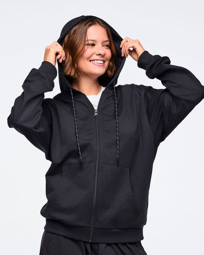 Front view of a female model pulling on the hood of a black zip-up hoodie, layered over a white top, paired with black pants, against a white background.