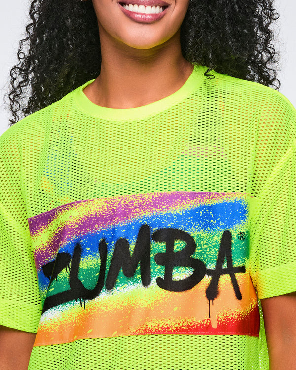 Close-up of a female model wearing a neon yellow Zumba mesh shirt with 'Zumba' in black text against a rainbow design.