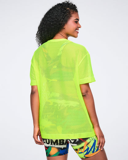 Back view of a female model wearing a bright yellow mesh shirt and colorful biker shorts on a white background.