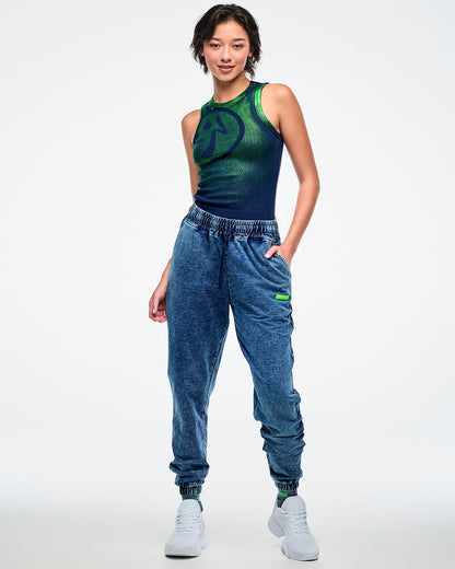 Full view of a female model wearing a green-to-blue gradient tank tucked into blue denim pants and paired with white shoes.