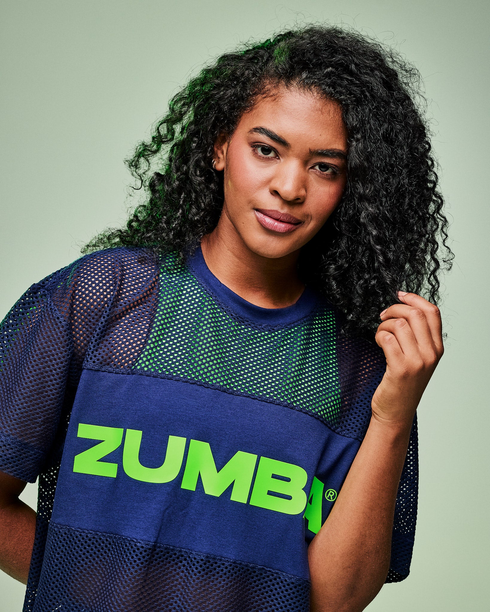 Close-up of a female model wearing an indigo Zumba-branded mesh top layered over a green tank.