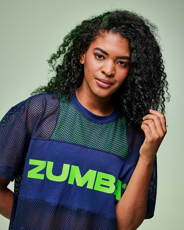 Close-up of a female model wearing an indigo Zumba-branded mesh top layered over a green tank.