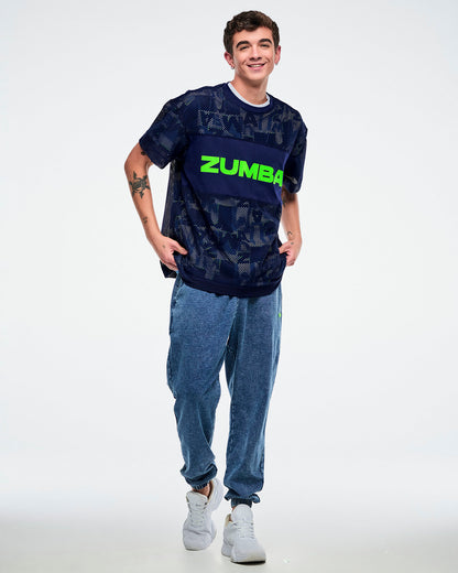 Male model wearing an indigo Zumba-branded mesh top paired with blue pants on a white background.