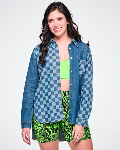 Front view of a female model wearing an open denim button-down with a checkerboard front panel, layered over a neon green bra top and paired with green snake-skin biker shorts.