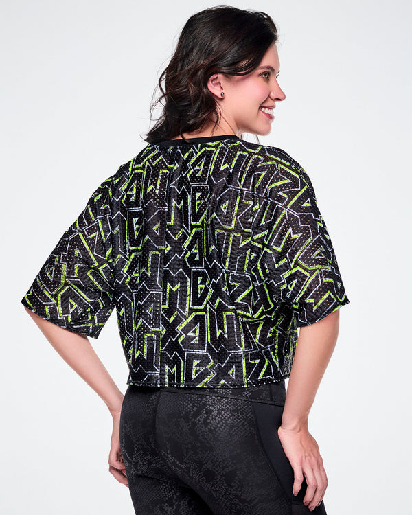 Back view of a female model wearing a short-sleeve mesh boxy crop top with rock-like letter patterning that says 
