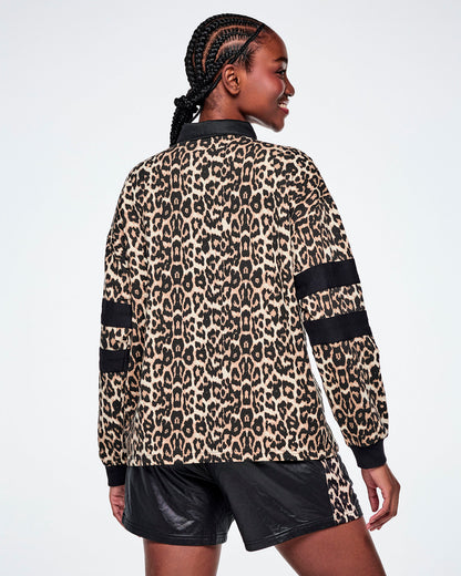Back view of a female model wearing a long-sleeve leopard-print polo shirt with black collar, cuffs, and sleeve stripes, paired with black shorts against a white background.