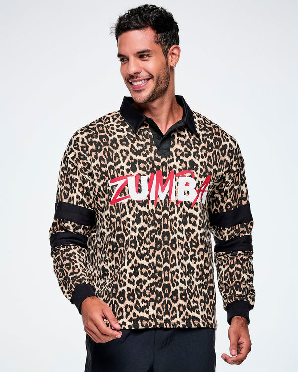 A male model wearing a long-sleeve leopard-print polo shirt with black collar, cuffs, and sleeve stripes, featuring red and white 'ZUMBA' text across the chest, paired with black pants against a white background.
