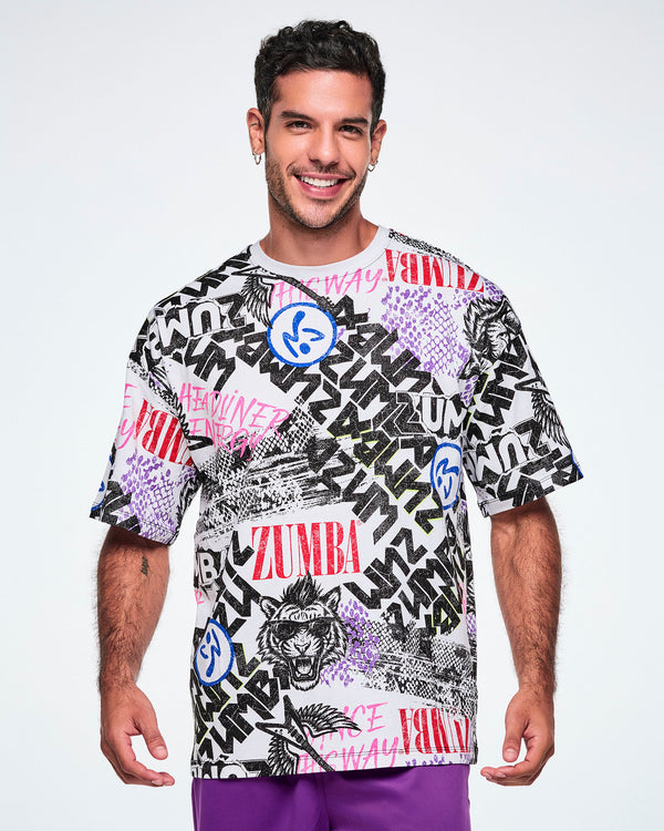 A smiling male model wearing a graphic tee with black, white, pink, and blue graffiti-style print and logos, such as blue zumbitos, a tiger wearing sunglasses, 