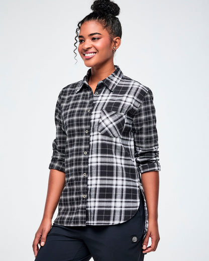 A woman modeling a black and white plaid button-down shirt with rolled-up sleeves, paired with black pants, against a white background.