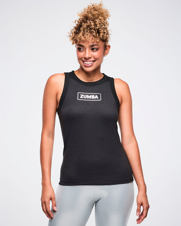 Female model wearing a black tank top with a silver 'Zumba' logo on the chest, paired with silver biker shorts.