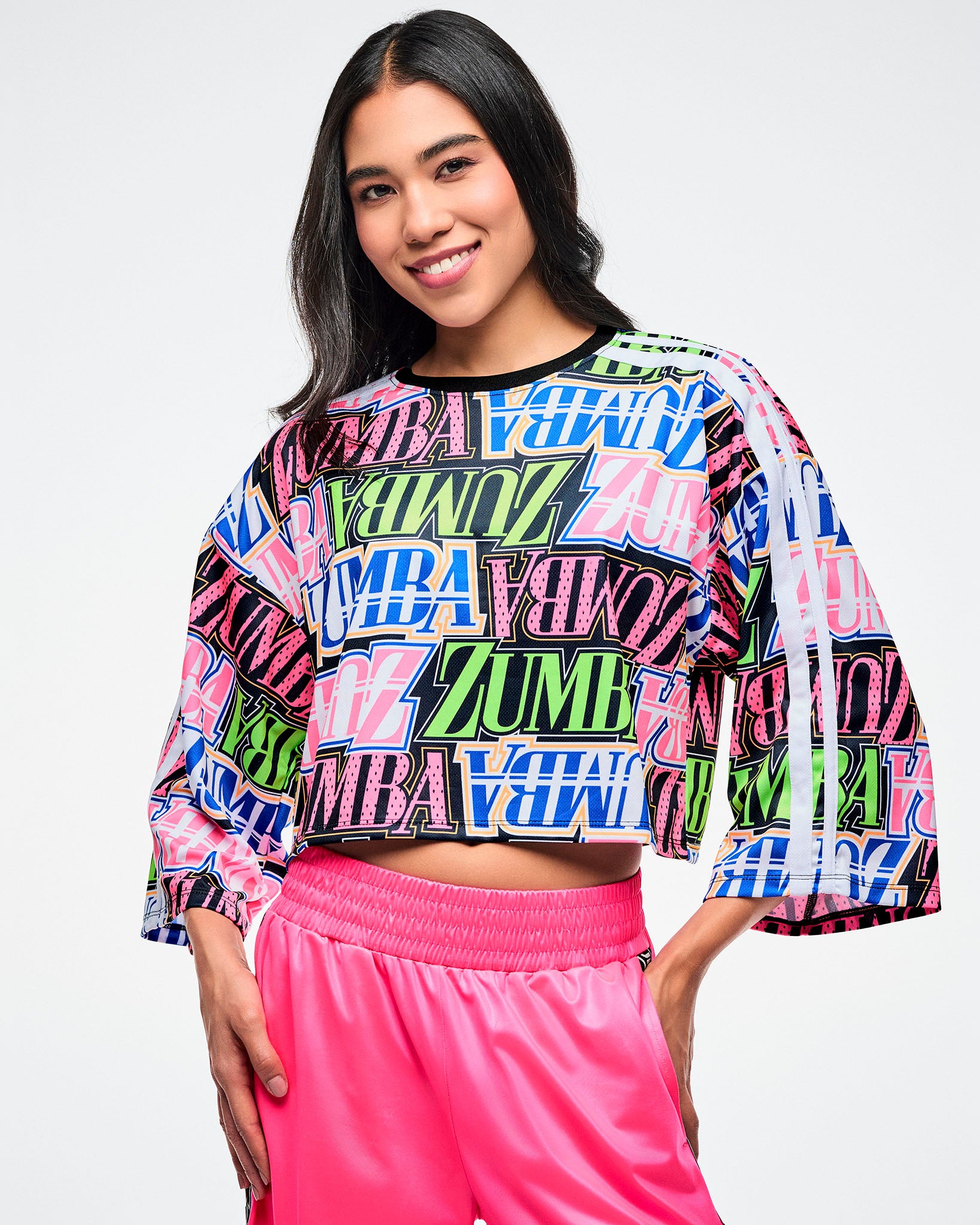 Female model wearing a colorful Zumba boxy crop top and pink pants on a white background.