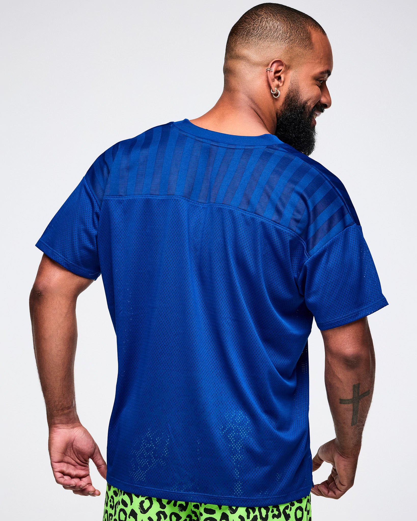 Back view of a male model wearing a blue mesh jersey with green leopard pants.