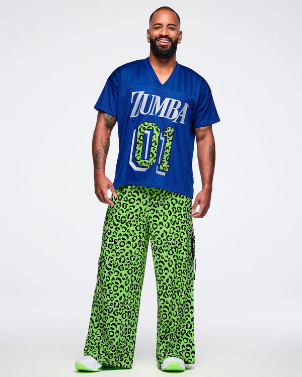 Male model wearing a blue jersey with 'ZUMBA 01' print paired with green leopard pants and green and white shoes.
