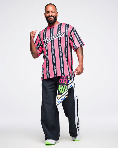 Male model wearing a pink-and-black striped Zumba top with white cursive “Zumba,” black-and-white striped pants, green-and-white shoes, and a bandana tucked into his pants.