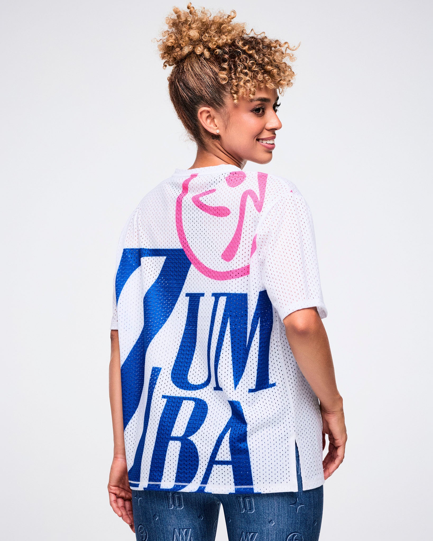 Back view of a white mesh top featuring a large pink Zumbito and bold blue “Zumba” text covering most of the back.