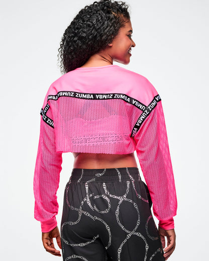 Back view of a female model wearing a pink Zumba crop top and black patterned pants on a white background.