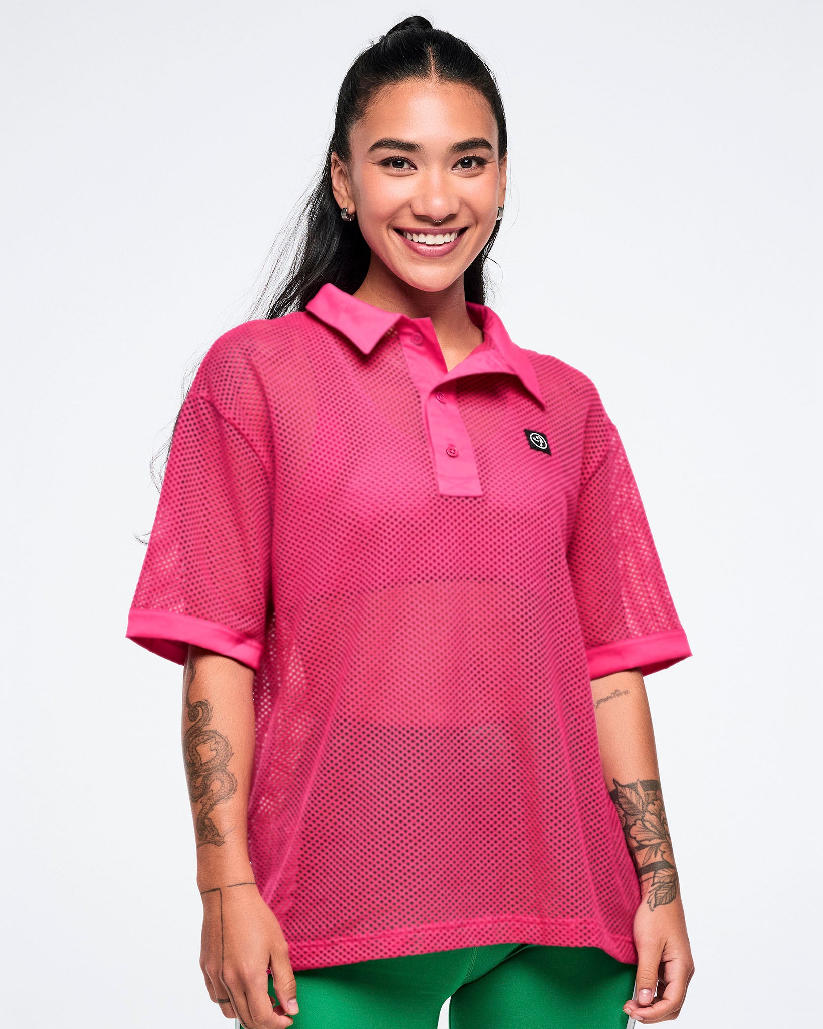 Female model wearing a pink mesh polo with a brand logo on a white background.