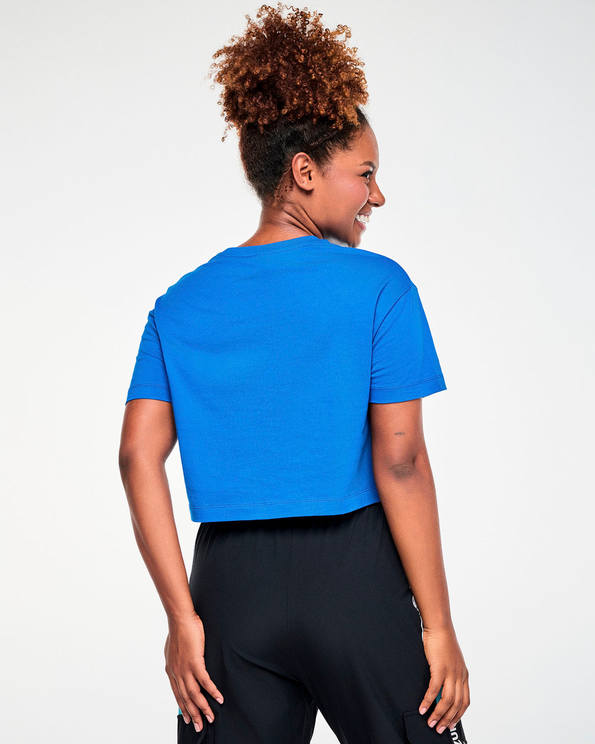 Shown from the back, a female model in the blue Smurfette graphic crop top, with a plain back and a relaxed, boxy fit.