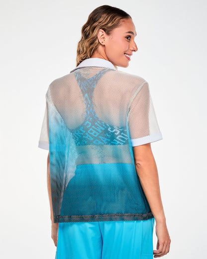 Shown from the back, a female model in the white-to-blue mesh polo, with the print bra's racerback visible through the sheer mesh.
