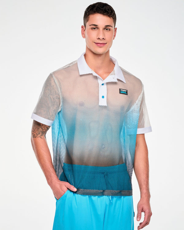 Male model in an oversized, sheer honeycomb mesh polo shading from white at the shoulders to light blue and dark blue at the hem, with a white collar, placket, and sleeve cuffs, light blue buttons, and a 'ZUMBA' X 'THE SMURFS' patch on the left chest. Paired with aqua blue cargo pants.