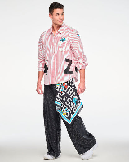 Male model in the red and white striped button-up with the embroidered Smurf on the chest pocket and black 'ZUMBA' letters at the hem, paired with black tonal logo print wide-leg pants and a Smurfs bandana hanging at the hip.