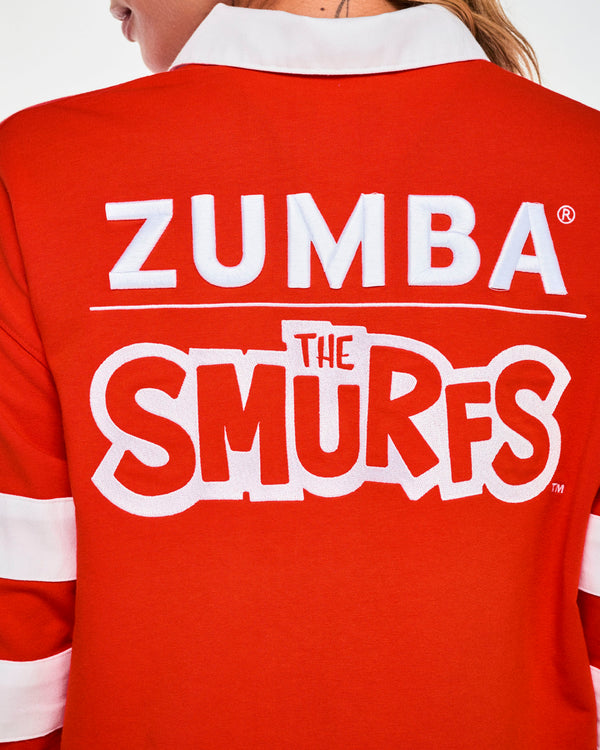 Close-up of the polo's back, showing raised white 'ZUMBA' lettering, a thin white rule, and 'THE SMURFS' logo in red letters outlined in white, just below the white collar.