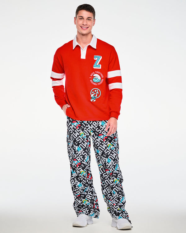 Male model smiling with one hand in his pocket, in the red rugby polo with a white collar and sleeve stripes, paired with black and white Smurfs print cargo pants.