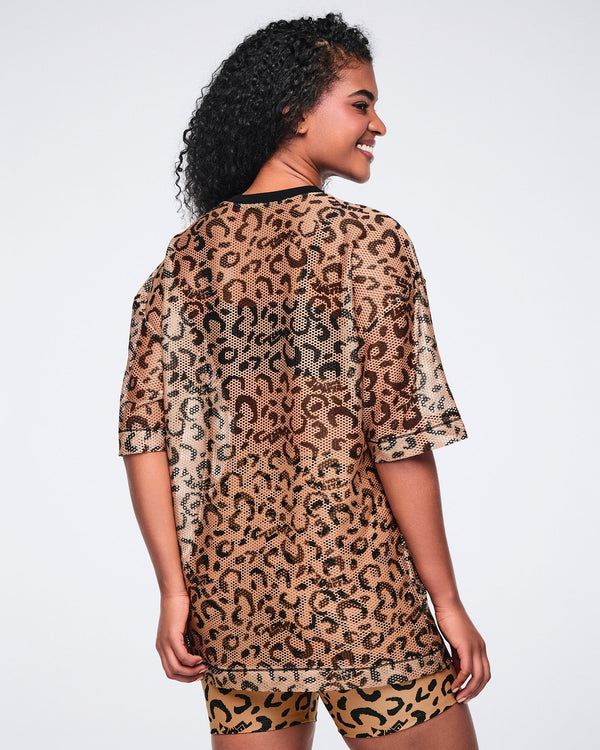 Tan leopard-print mesh top with black abstract spots, a black V-neck collar, oversized fit, and elbow-length sleeves, shown from the back on a smiling female model wearing matching leopard-print biker shorts.