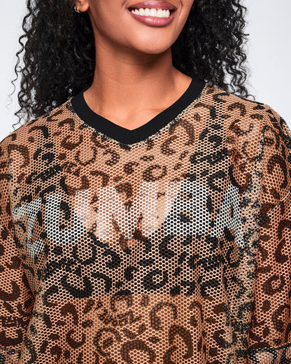 Close-up of a tan leopard-print mesh top with black abstract spots and a black V-neck collar, shown on a smiling female model.