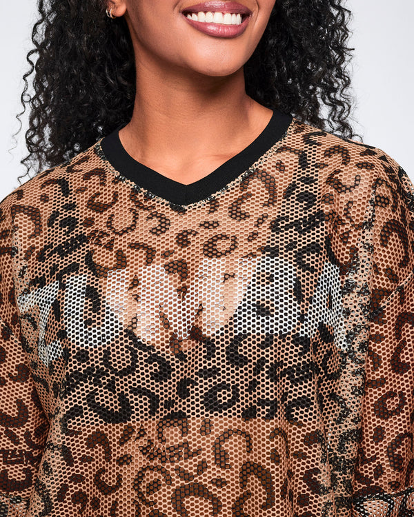 Close-up of a tan leopard-print mesh top with black abstract spots and a black V-neck collar, shown on a smiling female model.