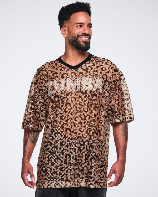 Tan leopard-print mesh top with black abstract spots, a black V-neck collar, oversized fit, and elbow-length sleeves, shown on a smiling male model wearing black long shorts.