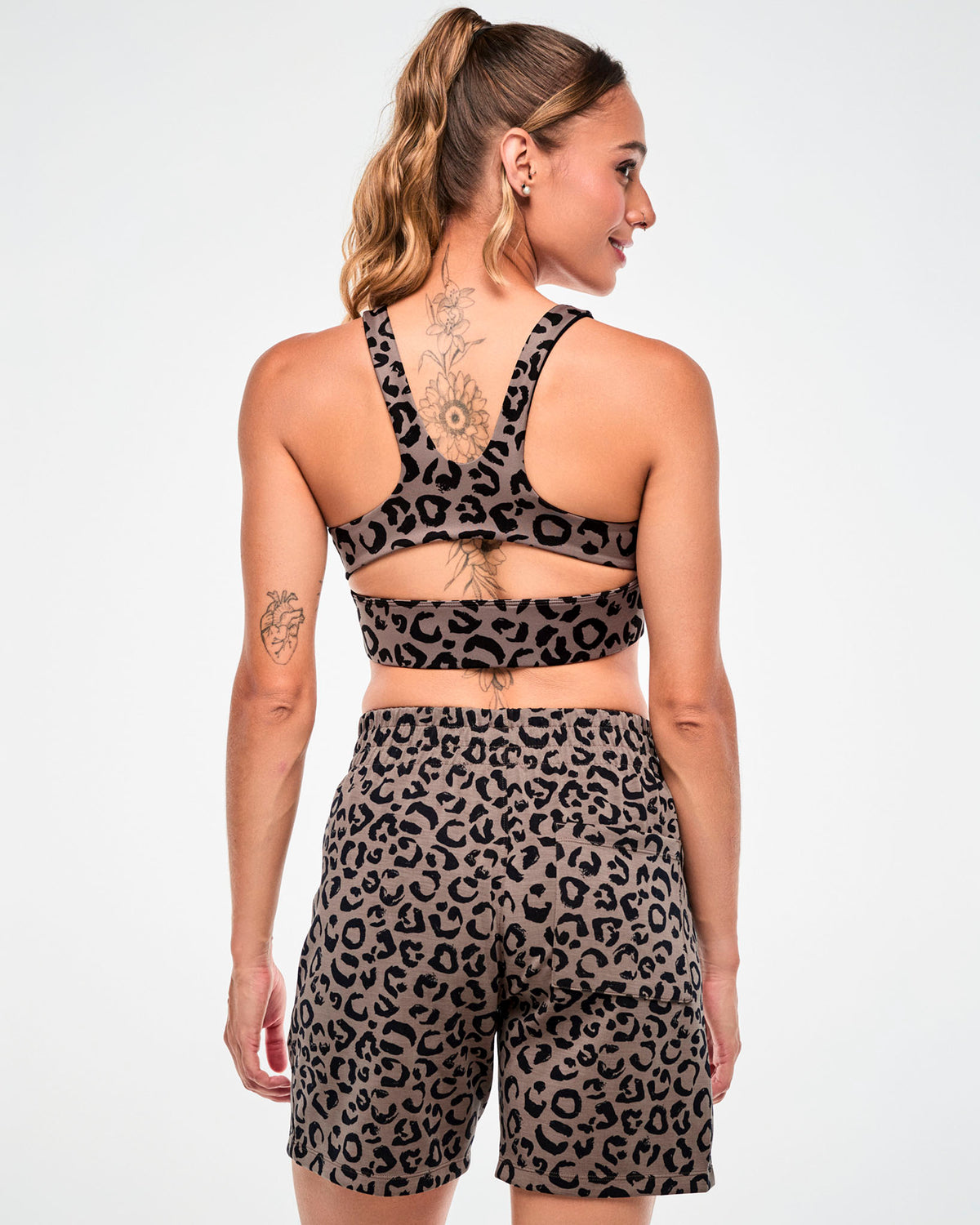 Back view of a female model in the brown leopard print racerback bra with a keyhole cutout, paired with matching leopard print shorts.