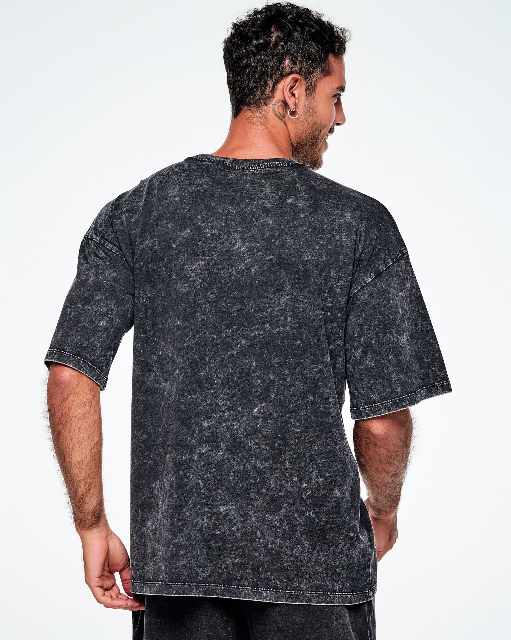 Back view of a male model wearing a black acid-wash graphic tee, paired with red and black leggings.
