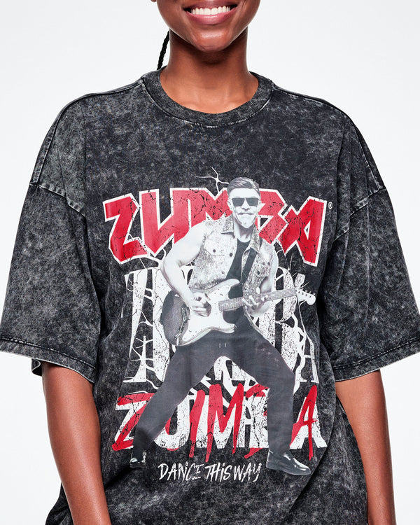 Close-up of the black acid-wash graphic tee with Beto, the creator of Zumba, smiling in sunglasses jamming on a guitar in black and white with ZUMBA in red and white text behind him and Dance this Way in smaller white text underneath.