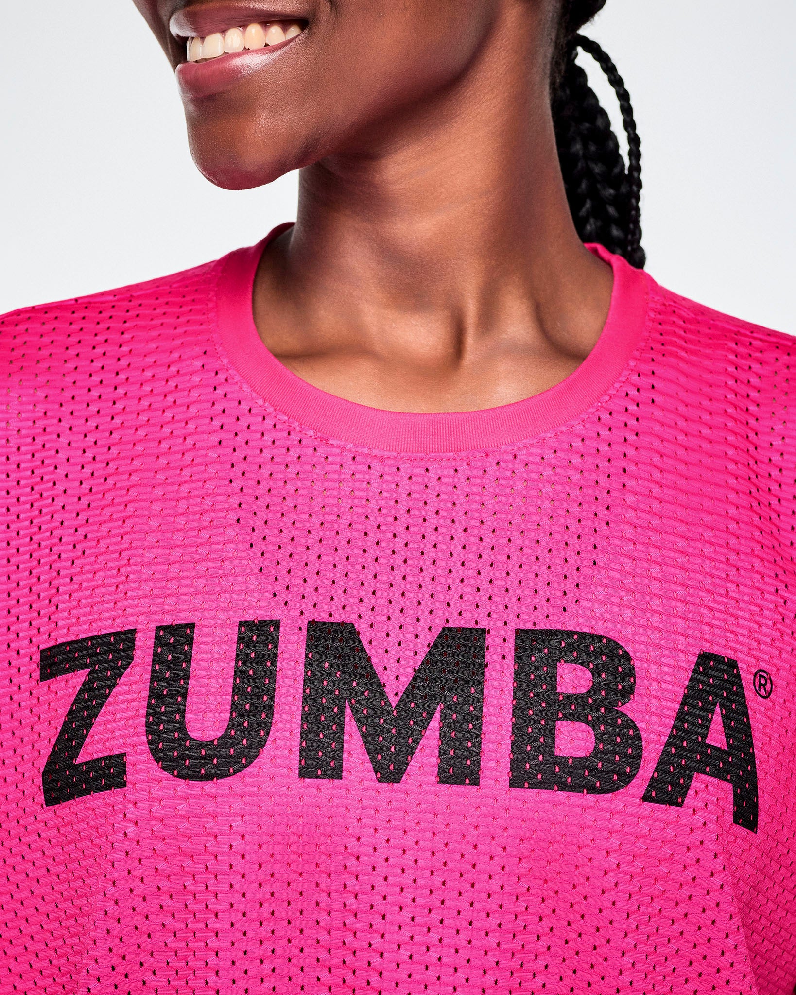 Close-up of a female model wearing a bright pink Zumba mesh top with a black ZUMBA lettering across the chest.