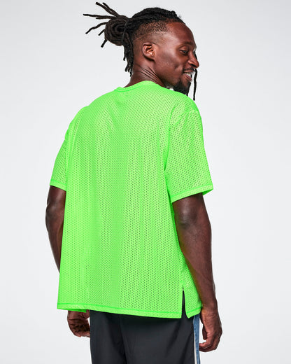 Back view of a male model wearing a neon green oversized mesh boxy top, paired with black backed blue denim pants, against a white background.