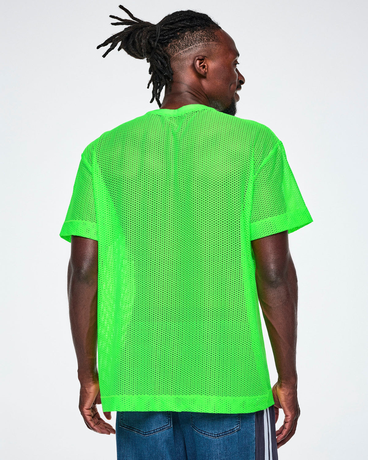 Back view of a male model wearing a bright green Zumba mesh top, paired with blue denim pants.