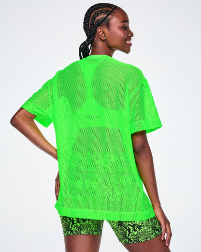 Back view of a female model wearing a bright green Zumba mesh top, paired with black and green ZUMBA snake-skin patterned biker shorts.