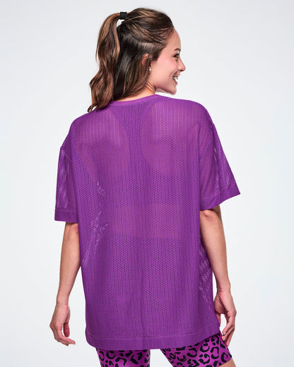 Back view of a female model wearing a purple Zumba mesh top, paired with black and purple leopard print biker shorts.
