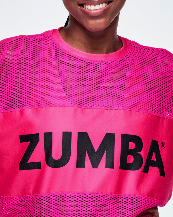 Close-up of a female model wearing a bright pink Zumba mesh top with a large black ZUMBA letters across the chest.