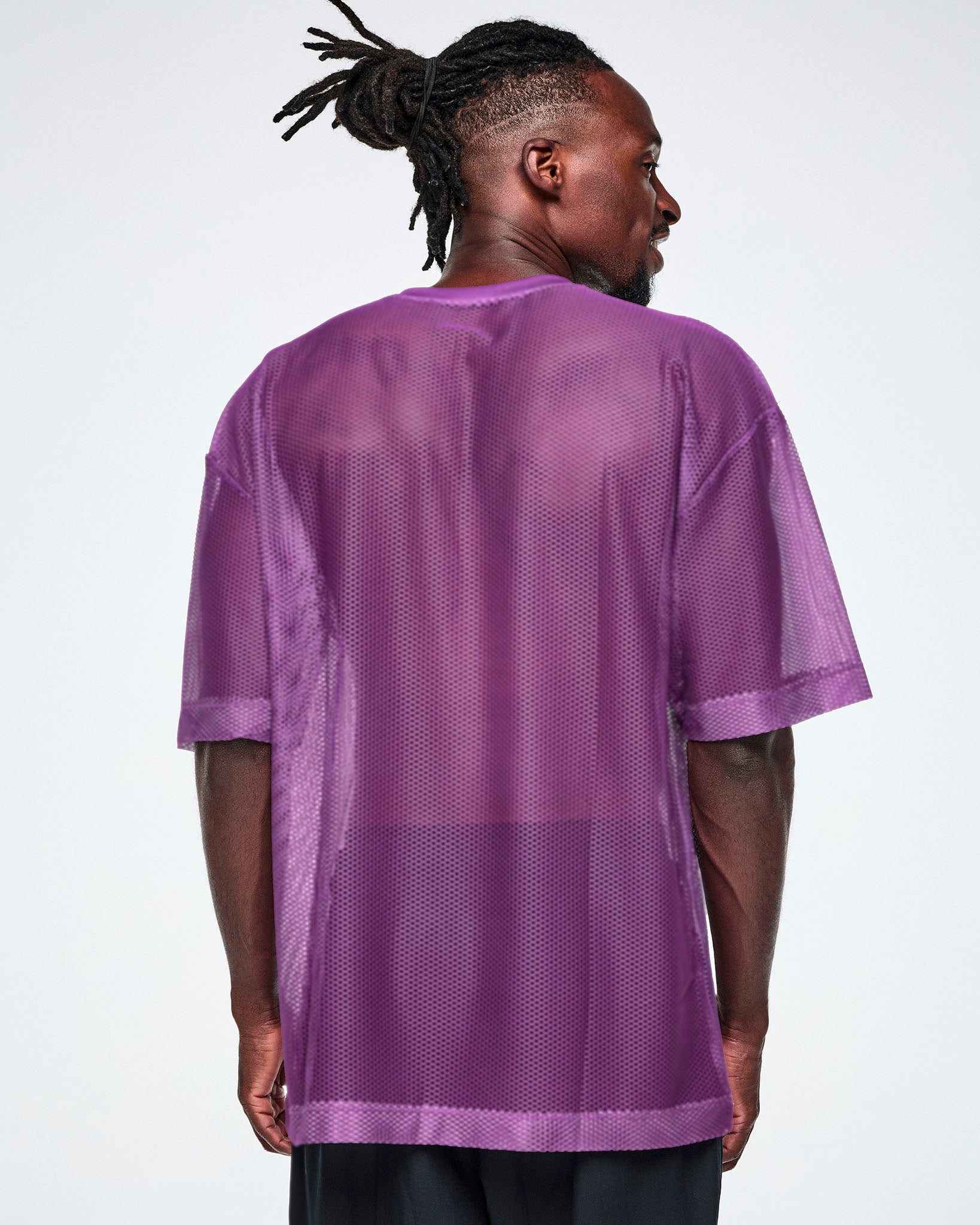 Back view of a male model wearing a purple mesh Zumba top, paired with black pants.