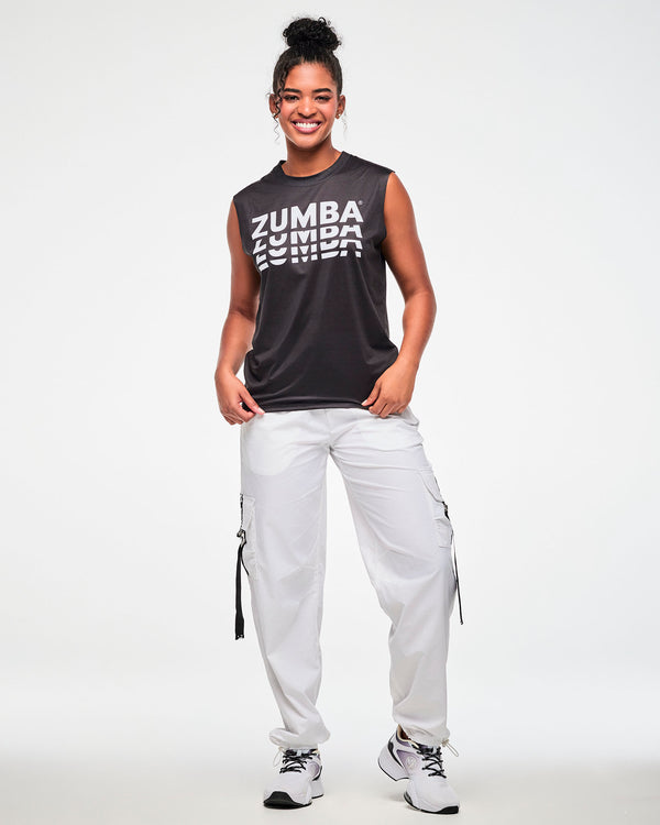 Black sleeveless muscle tee with a repeating white 'ZUMBA' logo, worn by a female model with white cargo pants and white shoes.