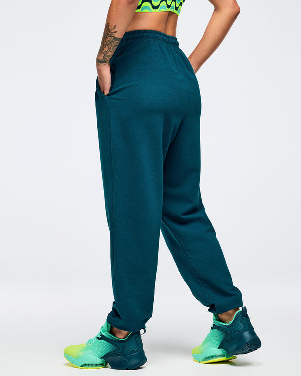 Teal jogger sweatpants with elastic drawstring waistband and a smooth back view, modeled by a female wearing teal-to-lime athletic sneakers on a white studio background.