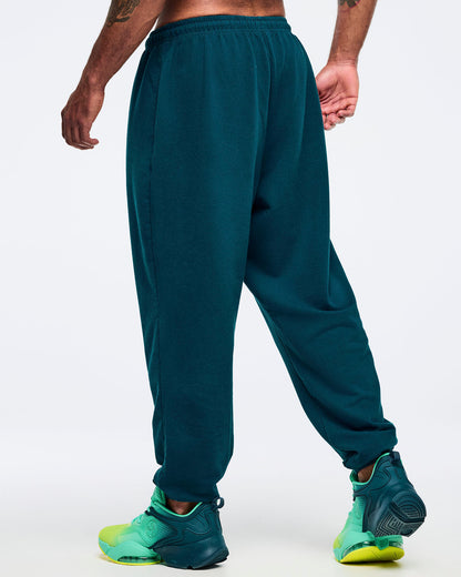 Teal jogger sweatpants with elastic waistband and relaxed tapered legs, shown from the back on a male model wearing teal-to-lime athletic sneakers on a white studio background.