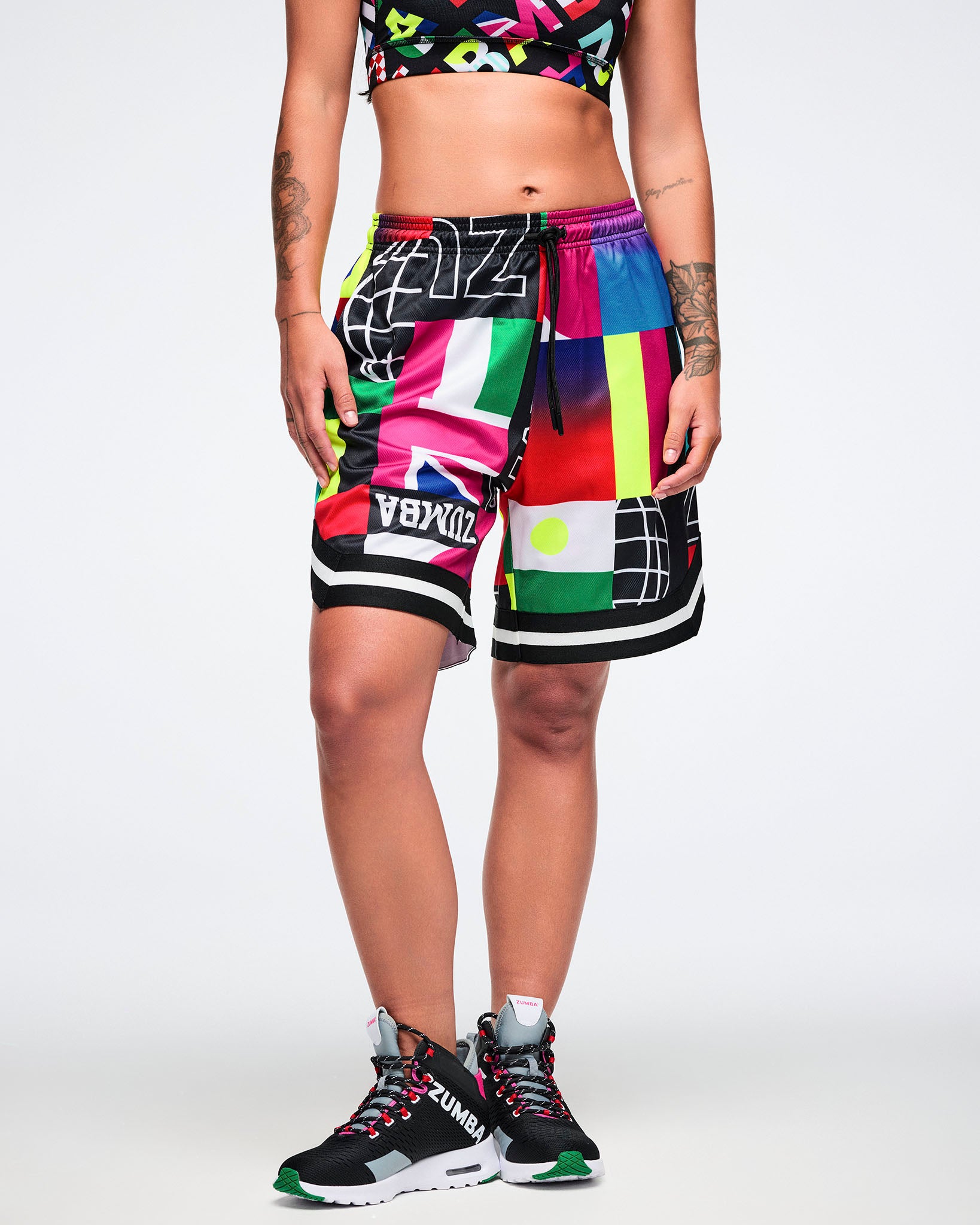 Female model wearing colorful patterned shorts and black sneakers on a white background.