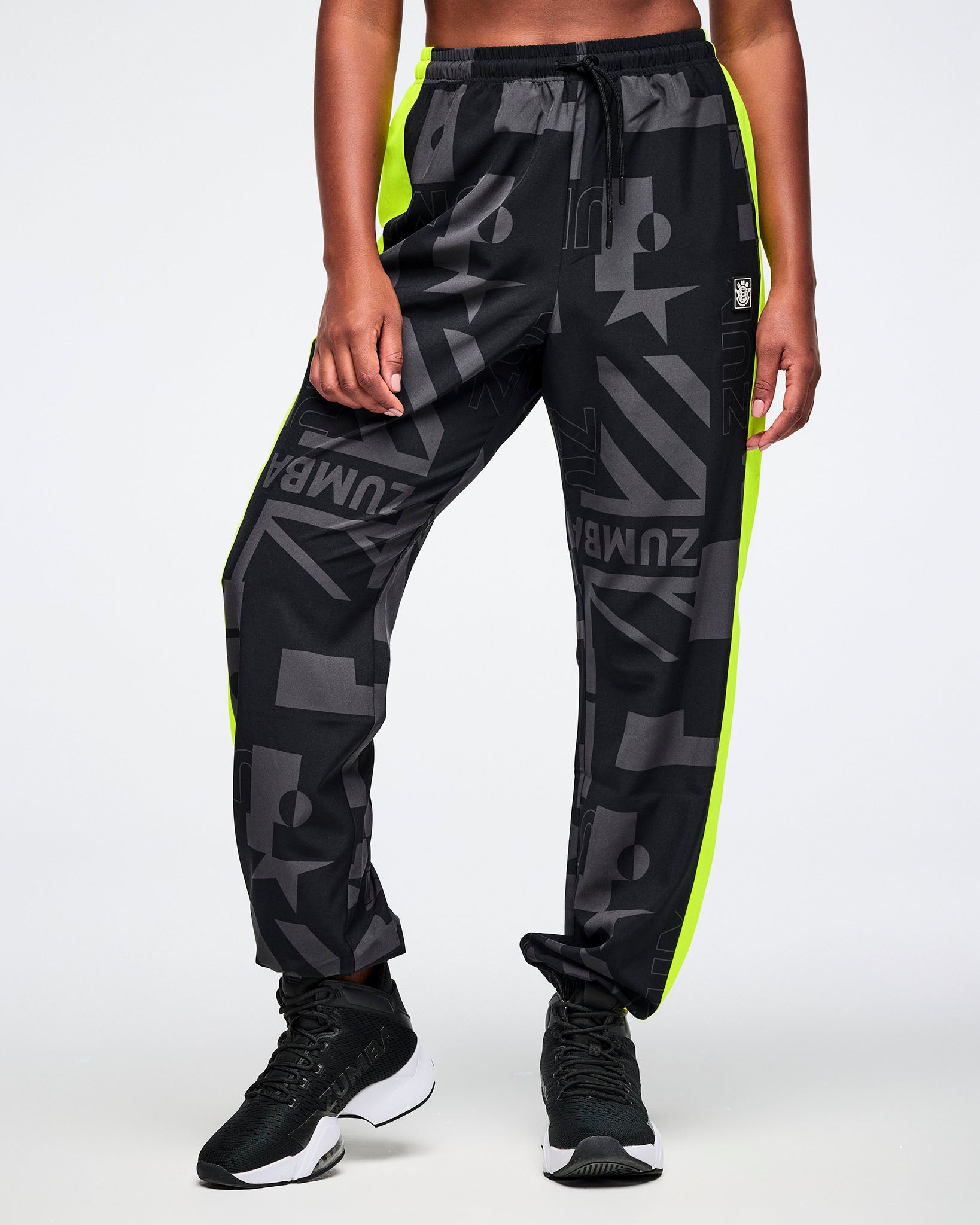 Female model wearing black and gray patterned pants with yellow stripes down the leg, worn by a person on a white background.