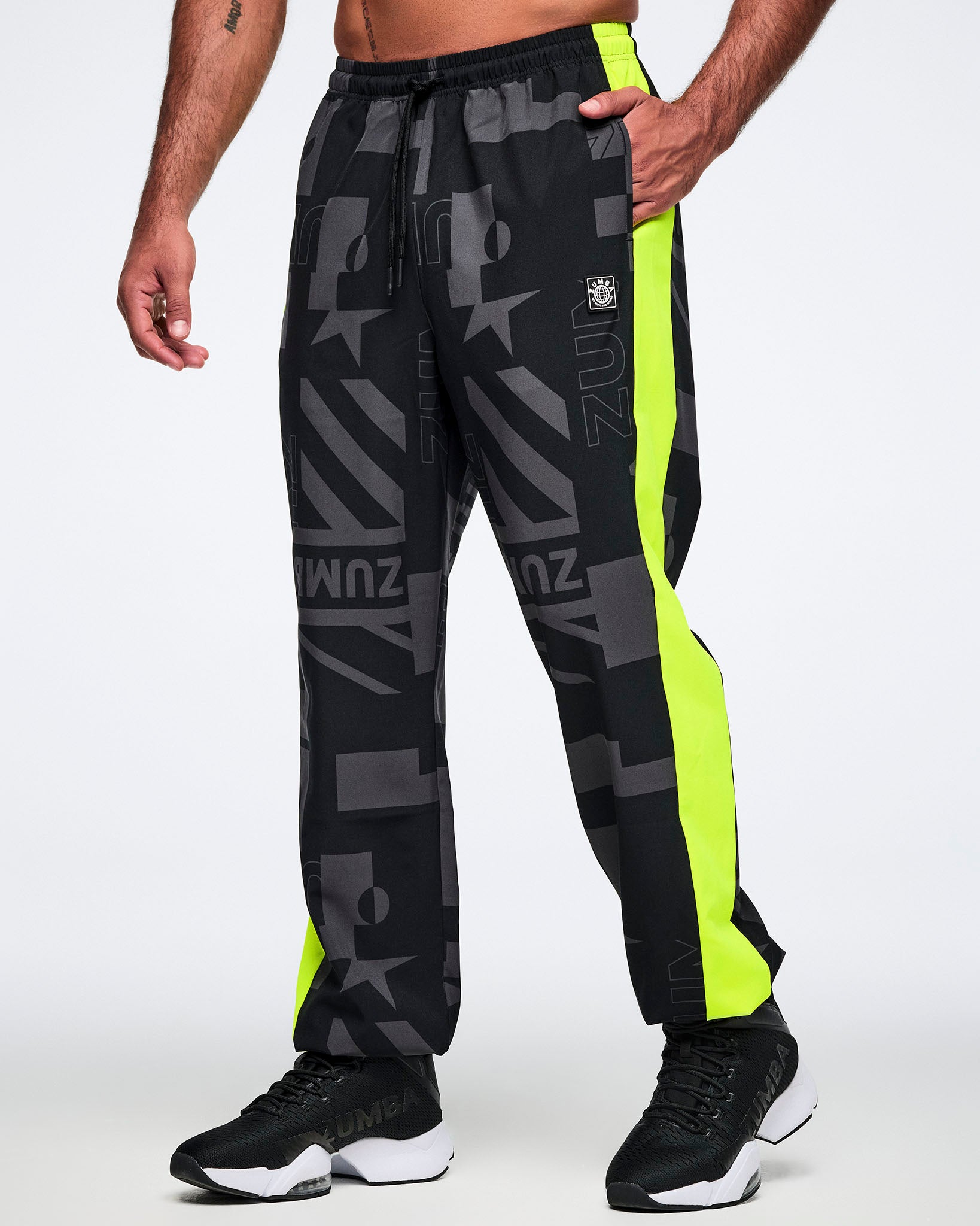 Male model wearing black and gray patterned pants with neon yellow stripes down both legs on a white background.